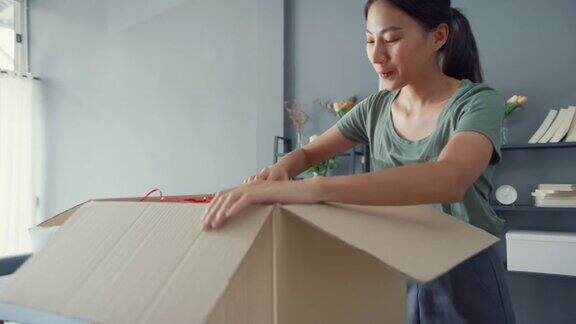 快乐美丽的亚洲女士打开纸箱从网上市场快递包裹在家里的客厅