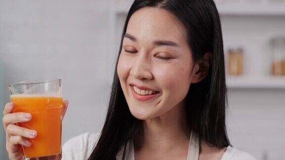 年轻的亚洲女子喝着橙汁拿着一杯橙汁微笑着看着镜头