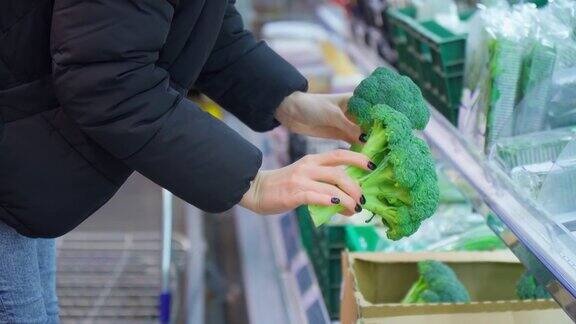 为了防止新冠肺炎疫情戴着医用口罩的妇女在超市选择蔬菜购买新鲜蔬菜花椰菜