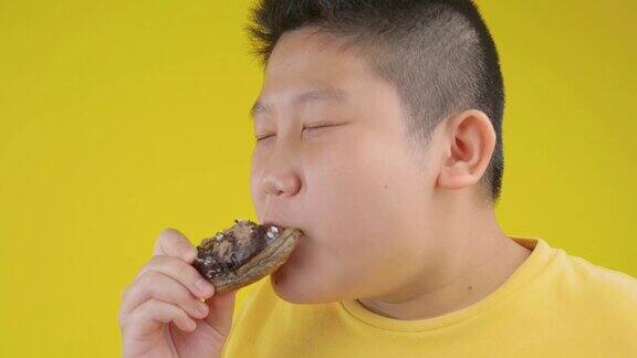 亚洲十多岁的男孩吃巧克力甜甜圈在黄色背景慢动作侧视图