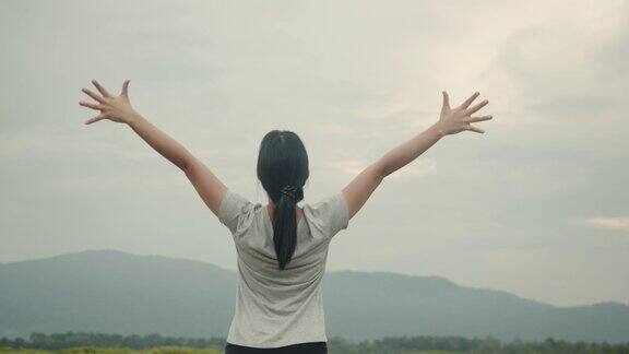 年轻的亚洲女子在运动服装高举在空中的山景感觉幸福