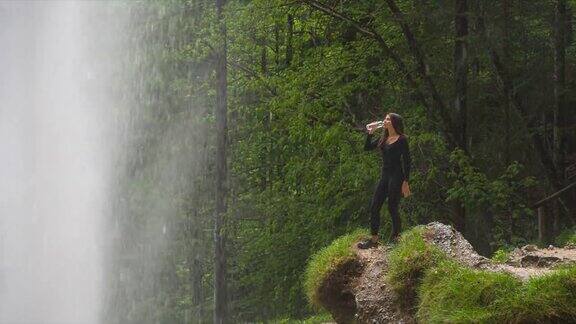 一名年轻女子在瀑布前喝水