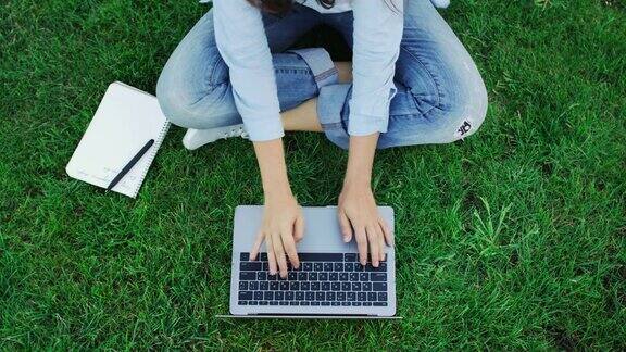 俯视图女人在笔记本键盘上打字而工作在公园的绿色草地上