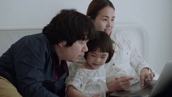 幸福的亚洲家庭和女儿在卧室使用笔记本电脑