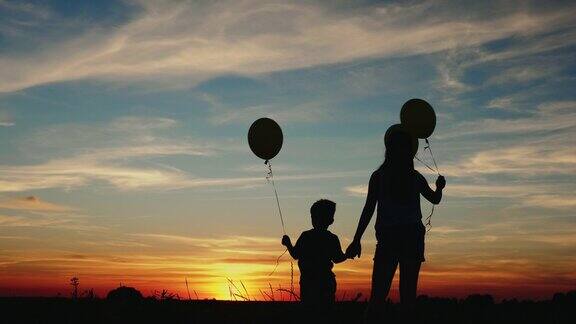 日落时两个拿着气球的孩子的剪影