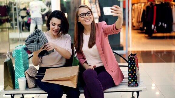 现代的年轻女性正在使用智能手机在购物中心进行在线视频通话女孩们边聊边笑展示买来的衣服挥舞着双手