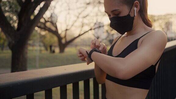 戴着防护口罩的女性正在为跑步设置健身智能手表女运动员检查手表装置