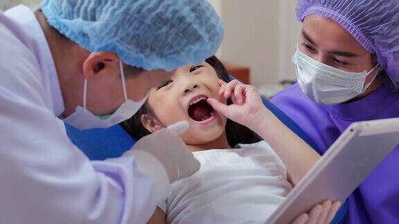 友善的医生和女婴在牙医办公室看平板电脑的肖像可爱的小女孩坐在牙科椅上正在进行牙科治疗医学、口腔医学和保健理念牙科检查、技术、教育、人