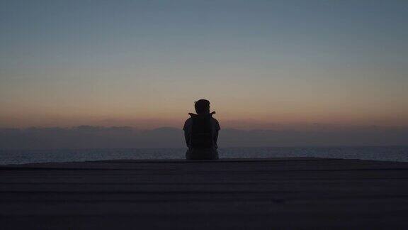 主题是孤独抑郁在旅行中寻找问题的答案一名背着背包的男子在帕福斯市塞浦路斯岛的木制码头上眺望地中海的日落