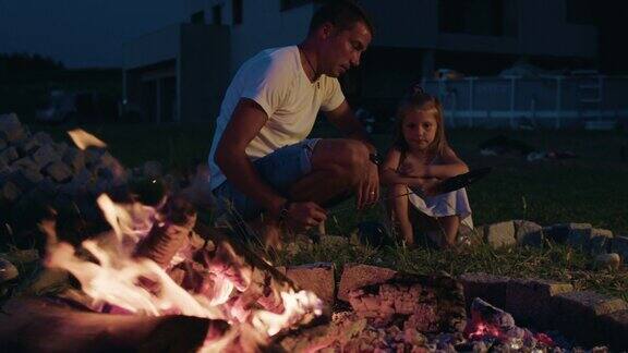 野营时父亲和女儿在篝火上烤玉米
