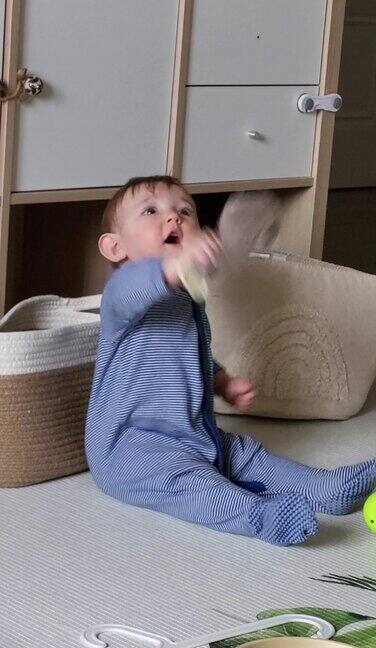 一个快乐的孩子坐在育儿室的地板上玩玩具宝宝在家里玩游戏时微笑9个月大的孩子
