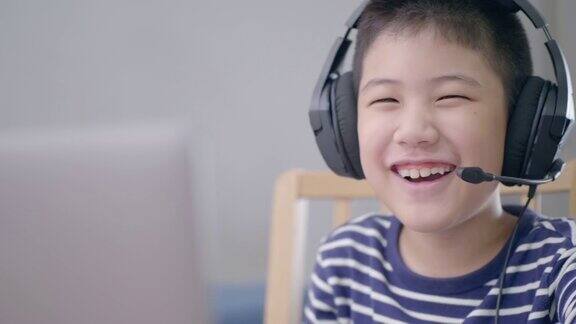 新常态亚洲男孩上网学习看着屏幕上的笔记本电脑开心的笑着在家里开心的笑着科技教育理念在家办公