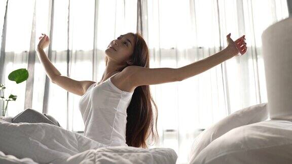 女人早上醒来后在床上伸展身体在卧室的大窗户背景上