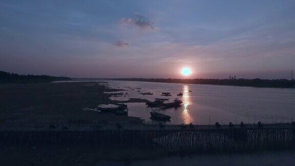 空中摇摄的汽车和摩托车在日落时穿过一条河上的竹桥
