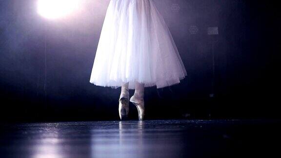 白色芭蕾舞演员的腿后面是一个黑色的舞台