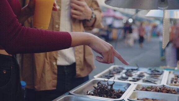 亚洲夫妇游客在街头小吃买炒昆虫