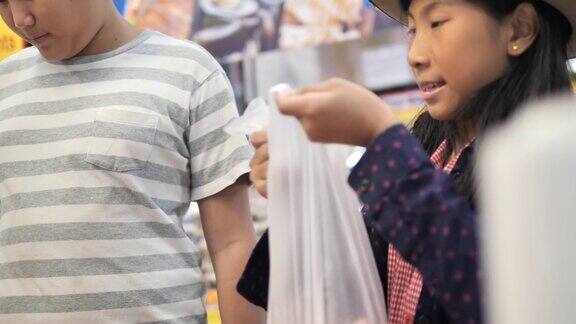 亚洲女孩和她的兄弟选择猪肉和放入袋子购物