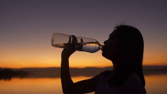 年轻女性在日落时喝水