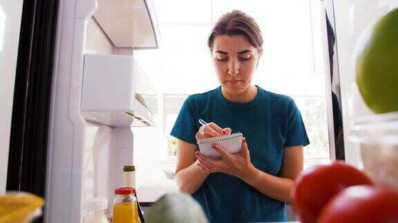 女人在冰箱里列出必要食物清单