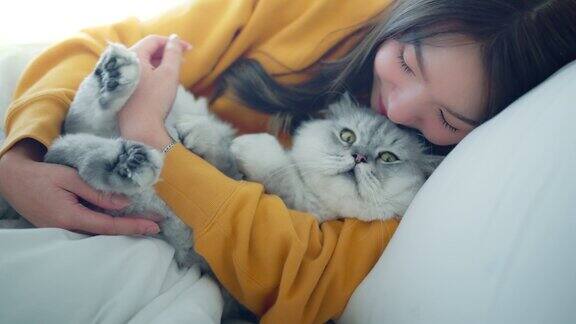 快乐的亚洲女人抱着毛茸茸的灰猫放松地躺在家里的床上宠物和主人之间的感人时刻宠物的友谊