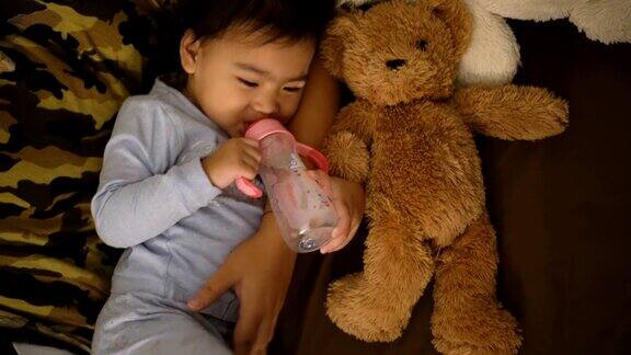 亚洲女孩用奶瓶喝牛奶抱着泰迪熊
