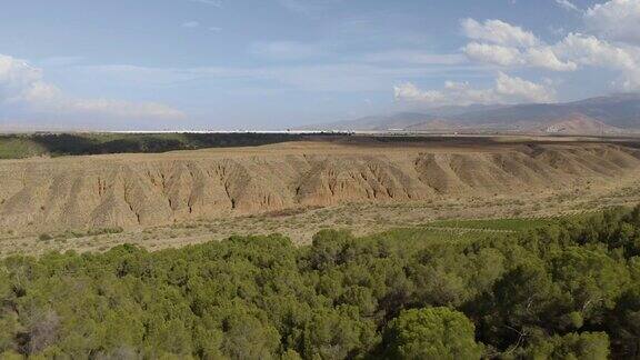 无人机拍摄的干燥峡谷在塔伯纳斯沙漠与绿色植被和山脉背景在安达卢西亚西班牙阿尔梅里亚的蓝天在白天岩石谷4K超高清内华达山脉