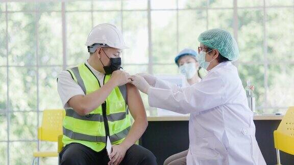 建筑行业新型冠状病毒疫苗接种站医生正在医院为团队工程工人接种疫苗以保护COVID-19或流感人们戴口罩以防御病毒健康福利