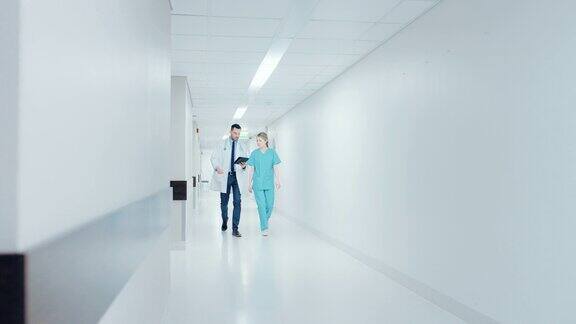 外科医生和女医生一边使用平板电脑一边匆忙地穿过医院走廊谈论病人的健康拥有专业人员的现代光明医院