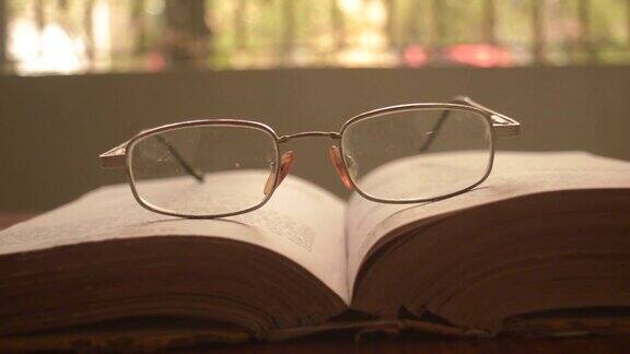 在一个温暖的阳光明媚的早晨将一本打开的书和一副眼镜或眼镜放在木桌上正面特写孤立的背景假日教育设计理念
