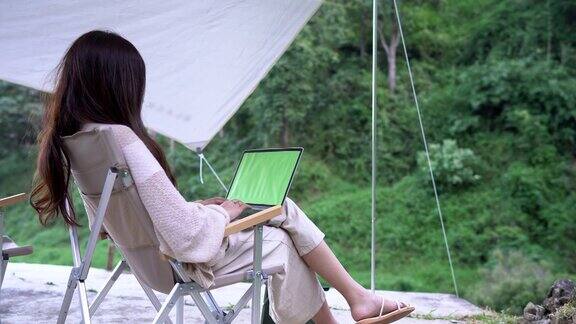 亚洲妇女工作在笔记本电脑的绿色屏幕上坐在椅子上在野外露营色度键
