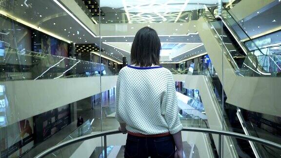 一个女人在购物中心爬上电梯从后面看