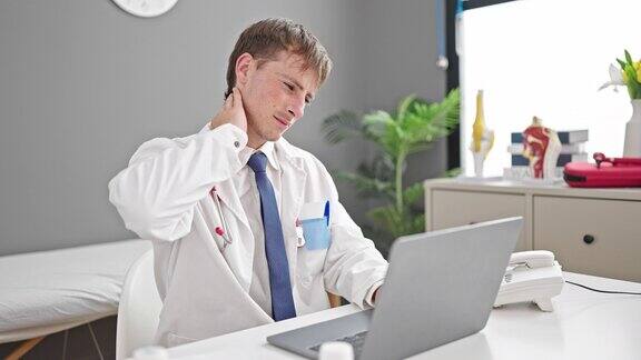 年轻的白人医生在诊所使用笔记本电脑强调颈椎疼痛