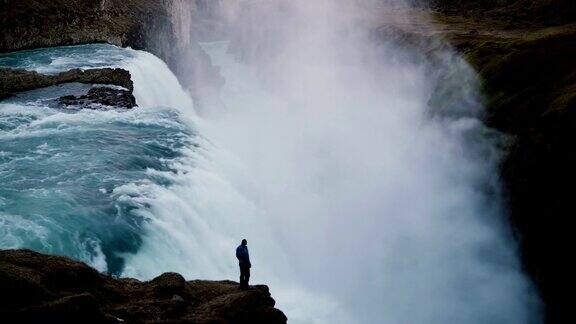 一个人站在岩石的边缘看着冰岛的海湾瀑布