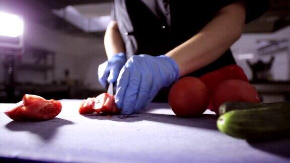 手戴手套的厨师用刀在砧板上切西红柿