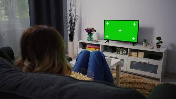 坐在家里的沙发上看绿色电视的女人