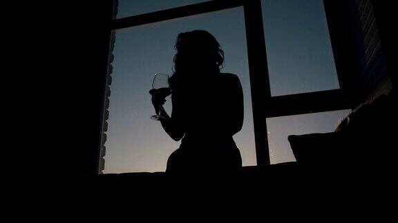 窗台上女孩摇晃酒杯的剪影