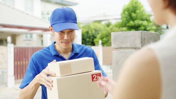 年轻的亚洲邮政快递员穿着蓝色衬衫处理包裹盒寄给客户在家里和亚洲女性收到包裹在户外