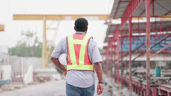 后面的观点非裔美国工程师或承包商或工头具有领导能力和专业知识穿着安全制服步行准备在建筑工地或住房项目工作工人正在房地产建设行业工作