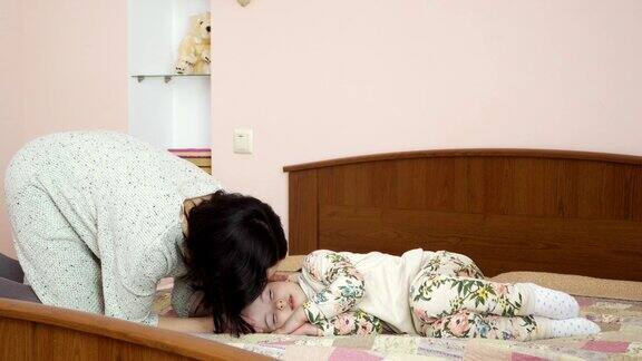 当小女儿在床上睡觉时年轻的母亲亲吻她的前额