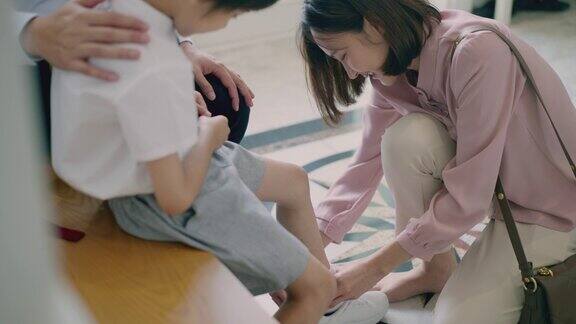 微笑的亚洲母亲系儿子的鞋带而可爱的小男孩玩和咬他的领带校服早上父母正在为他们上小学的儿子准备上学