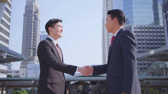 背景中亚洲商人在城市建筑中握手完成谈判后合作协议即为成功商业交易合并和收购概念