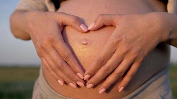 孕妇用她的手在她的胃上形成一个心在阳光日落