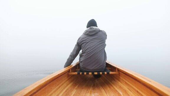 在雾蒙蒙的湖面上划着独木舟的人