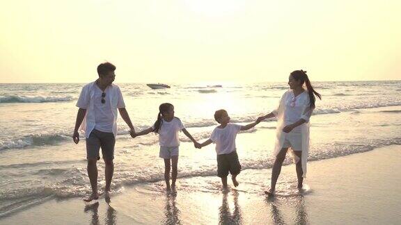 慢镜头剪影的年轻亚洲家庭父母与两个孩子的男孩和女孩走在海滩上与微笑一起在夏季日落快乐的家庭在假期放松和乐趣