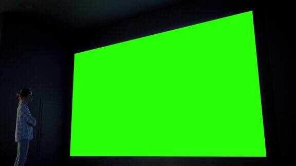 女人看着大空白绿色屏幕在黑暗的房间-色度键概念