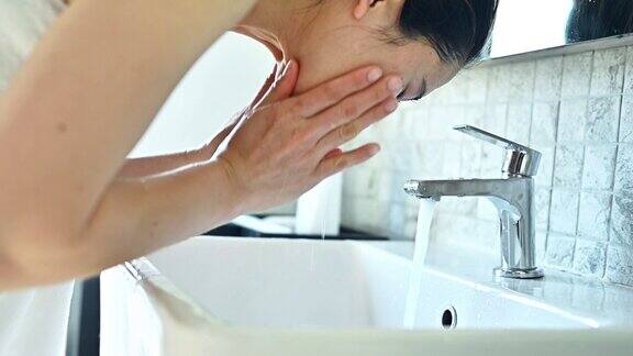一名亚洲妇女在浴室水槽边用水洗脸