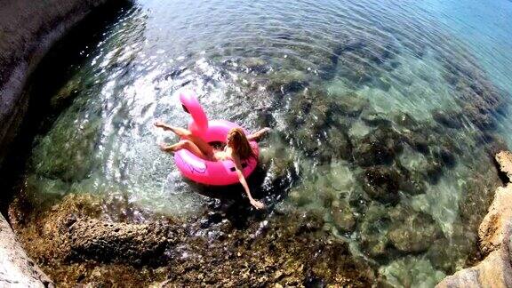 年轻苗条的女子享受大海和太阳躺在一个充气的粉红色火烈鸟