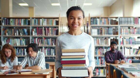 一个快乐的非裔美国妇女拿着书微笑着走进学校图书馆