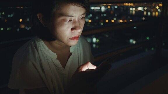 一个年轻的亚洲女人晚上用他的手机发短信