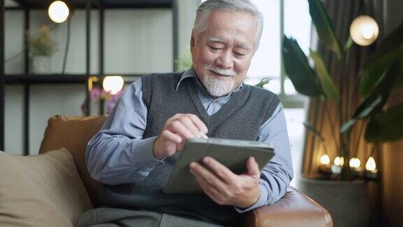 亚洲老人退休老人手使用平板电脑冲浪社交媒体浏览朋友在线社交交流距离连接幸福亚洲老人呆在家里使用平板电脑在家里